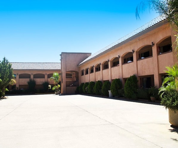 A building with a long corridor, arched windows, and potted plants.