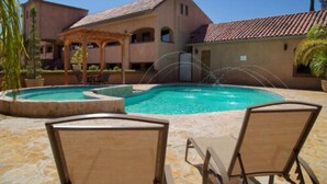 A pool area with lounge chairs, a pergola, and a building with a tiled roof. - Estancia Inn (Tecate)