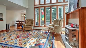 Un salon spacieux avec une grande fenêtre, une cheminée et un tapis à motifs.