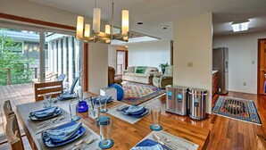 Un espace repas moderne avec une table en bois dressée pour quatre personnes, un lustre et une vue sur le salon en arrière-plan.