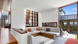 Un salon moderne avec un canapé d’angle, un mur décoratif en bois et de grandes fenêtres.
