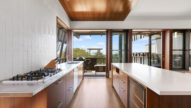 Une cuisine moderne dotée d’un îlot central, de meubles en bois et de grandes fenêtres offrant une vue sur l’extérieur.