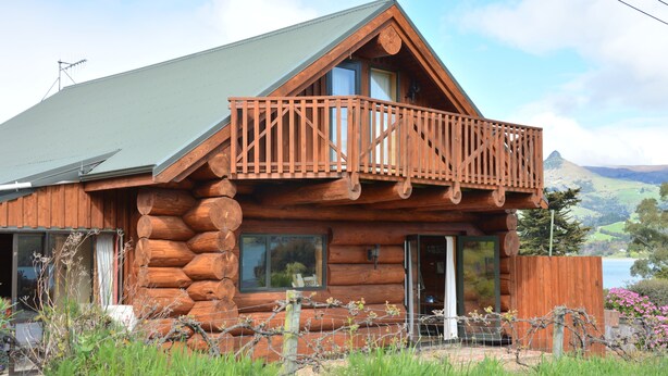 A log cabin with a balcony, large windows, and a view of a lake and mountains. - Log Cabin Vacation Retreat (Port Levy)