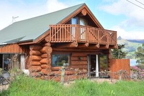 A log cabin with a balcony, large windows, and a view of a lake and mountains. - Log Cabin Vacation Retreat (Port Levy)
