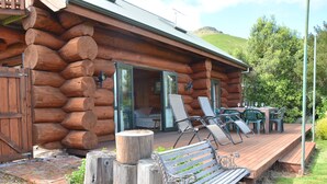 A log cabin with a deck, outdoor seating, and a view of the surrounding landscape. - Log Cabin Vacation Retreat (Port Levy)