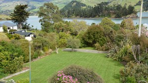 A lush garden with a lawn, a variety of trees, and a lake in the background. - Log Cabin Vacation Retreat (Port Levy)