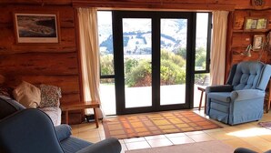A cozy living room with a blue sofa, a blue armchair, and a wooden coffee table. A large window offers a view of a mountainous landscape. - Log Cabin Vacation Retreat (Port Levy)