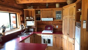 A compact kitchen with wooden cabinets, a red countertop, a microwave, a stove, and a sink. - Log Cabin Vacation Retreat (Port Levy)