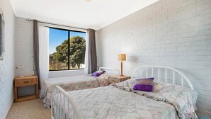 Ein Schlafzimmer mit zwei Betten, einem Fenster mit Vorhängen, einer Lampe und einem kleinen Tisch.