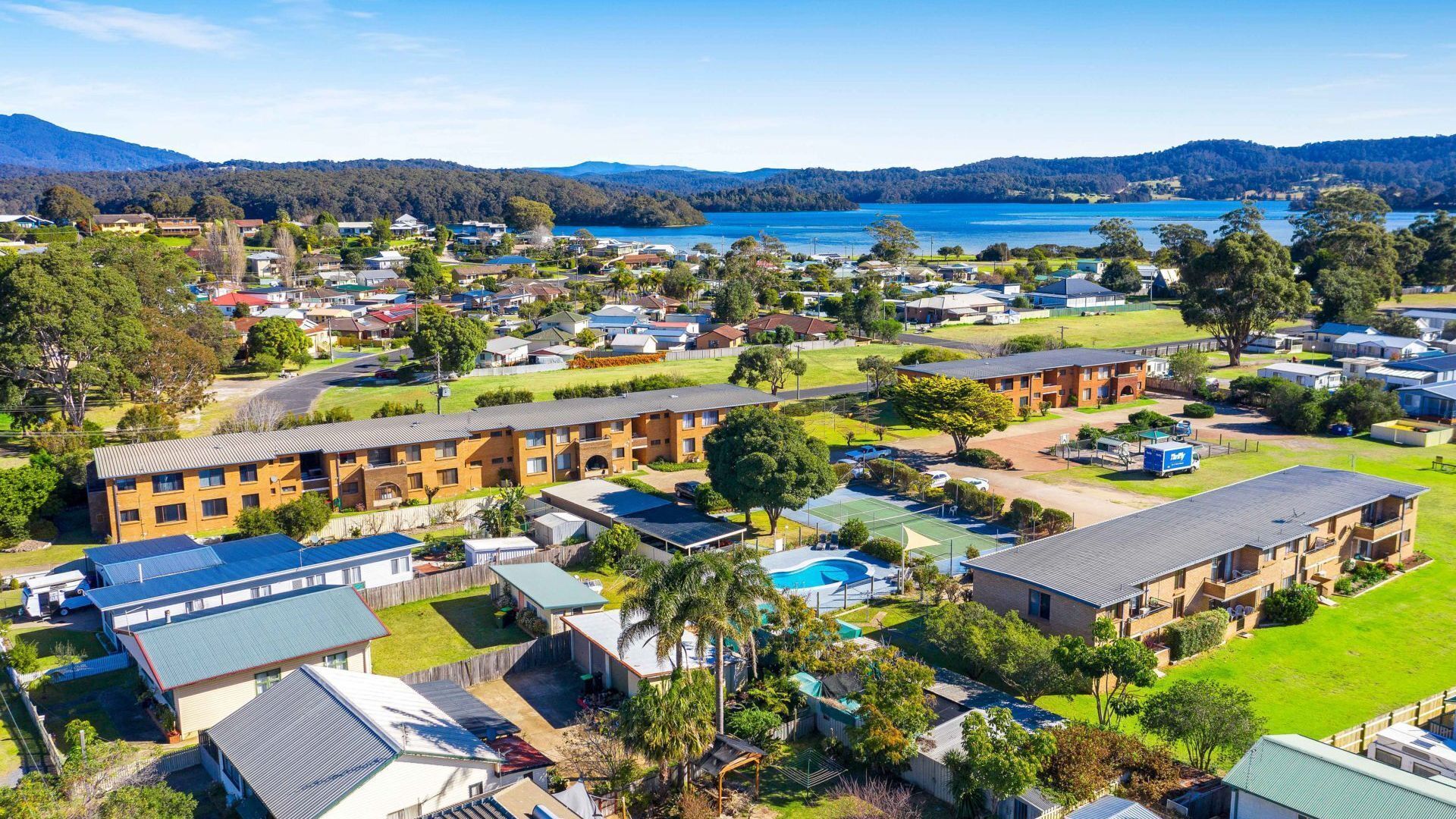 A residential area with multiple apartment buildings, a swimming pool, and a view of a lake and mountains.