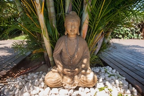 A seated Buddha statue surrounded by white pebbles and greenery. - Cabanas Prema (Imbituba)