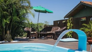 Une piscine agrémentée d’un élément décoratif aquatique, entourée d’une terrasse en bois, de mobilier d’extérieur et d’une végétation luxuriante.