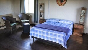 Une chambre à coucher comprenant un lit, deux fauteuils en osier, une petite table et un élément décoratif mural.