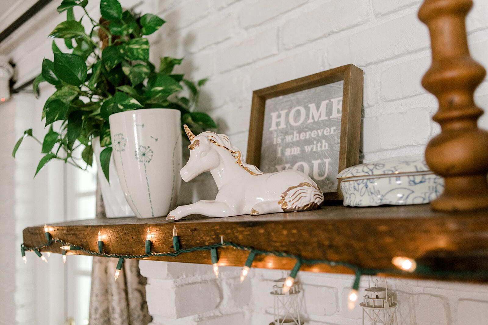 A shelf with a white unicorn figurine, a white ceramic pot with green floral patterns, a framed sign with the text "HOME is wherever I am with YOU", and a small blue and white ceramic container.