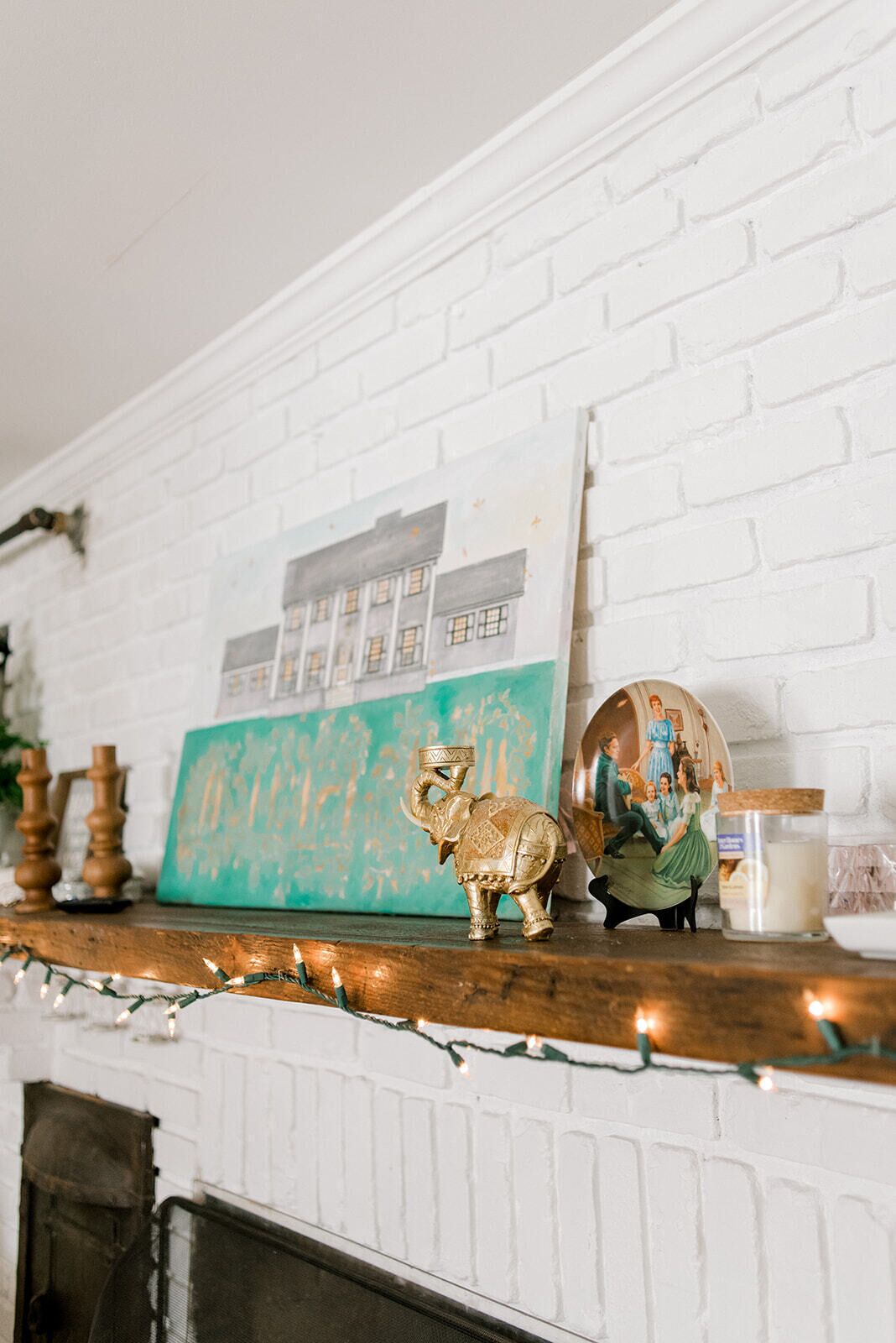 A white brick fireplace with a framed picture above it, a small elephant figurine, and a candle holder.
