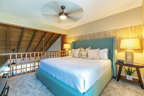 A bedroom with a large bed, two bedside lamps, a ceiling fan, and a view of the outdoors.