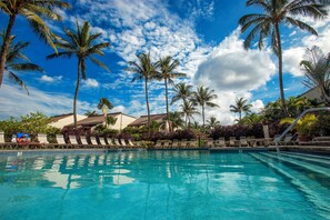 A pool area with clear blue water, surrounded by palm trees and lounge chairs.