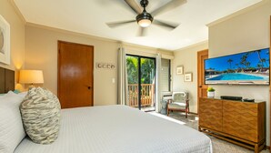 A hotel room with a large bed, a ceiling fan, a television displaying a pool, and a sliding glass door leading to a balcony. - Maui Kamaole #A-210 Panoramic Ocean View, Full A/C, Across Kamaole Bch III (Kihei)