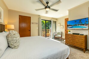 Camera d'albergo con un letto grande, una ventola a soffitto, un televisore che mostra una piscina e una porta scorrevole in vetro che dà su un balcone.