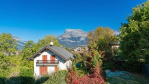 Una casa con balcón, rodeada de abundante vegetación y un paisaje montañoso.