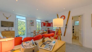Una sala de estar moderna con un sofá, una mesa con revistas, una lámpara y un televisor.
