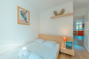 Una cama bien hecha con sábanas blancas y una toalla doblada, una lámpara de noche y un cartel enmarcado en la pared.