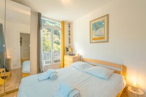 Ein Hotelzimmer mit Bett, Nachttisch, Spiegel, einem Fenster mit Vorhängen und einem gerahmten Bild an der Wand.