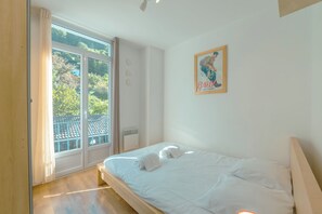 A bedroom with a bed, a window with curtains, a picture on the wall, and a view of the outside.
