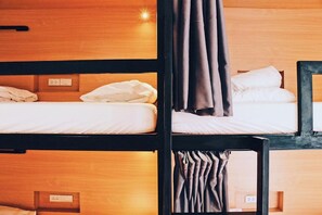 A bunk bed room with wooden headboards, white bedding, and a curtain on one bed.
