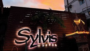 A hostel sign with a neon light, a wooden fence, and a palm tree. - Sylvis Hostel Chiangmai (Chiang Mai)