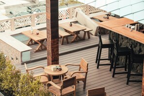 An outdoor patio with wooden tables and chairs, a brick wall, and a view of a street with parked scooters.