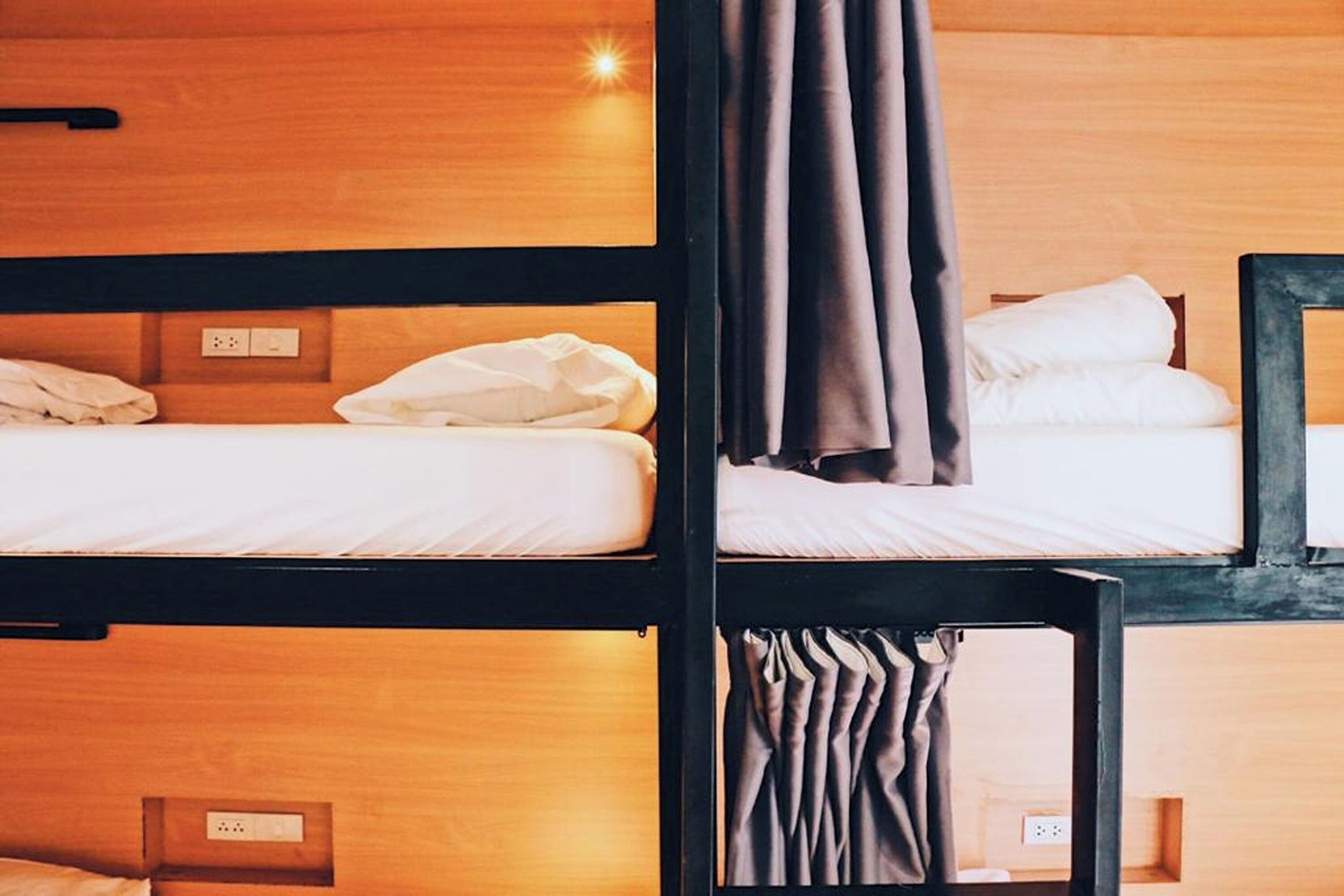 A bunk bed room with wooden headboards and a single bed with a white mattress and brown curtains.