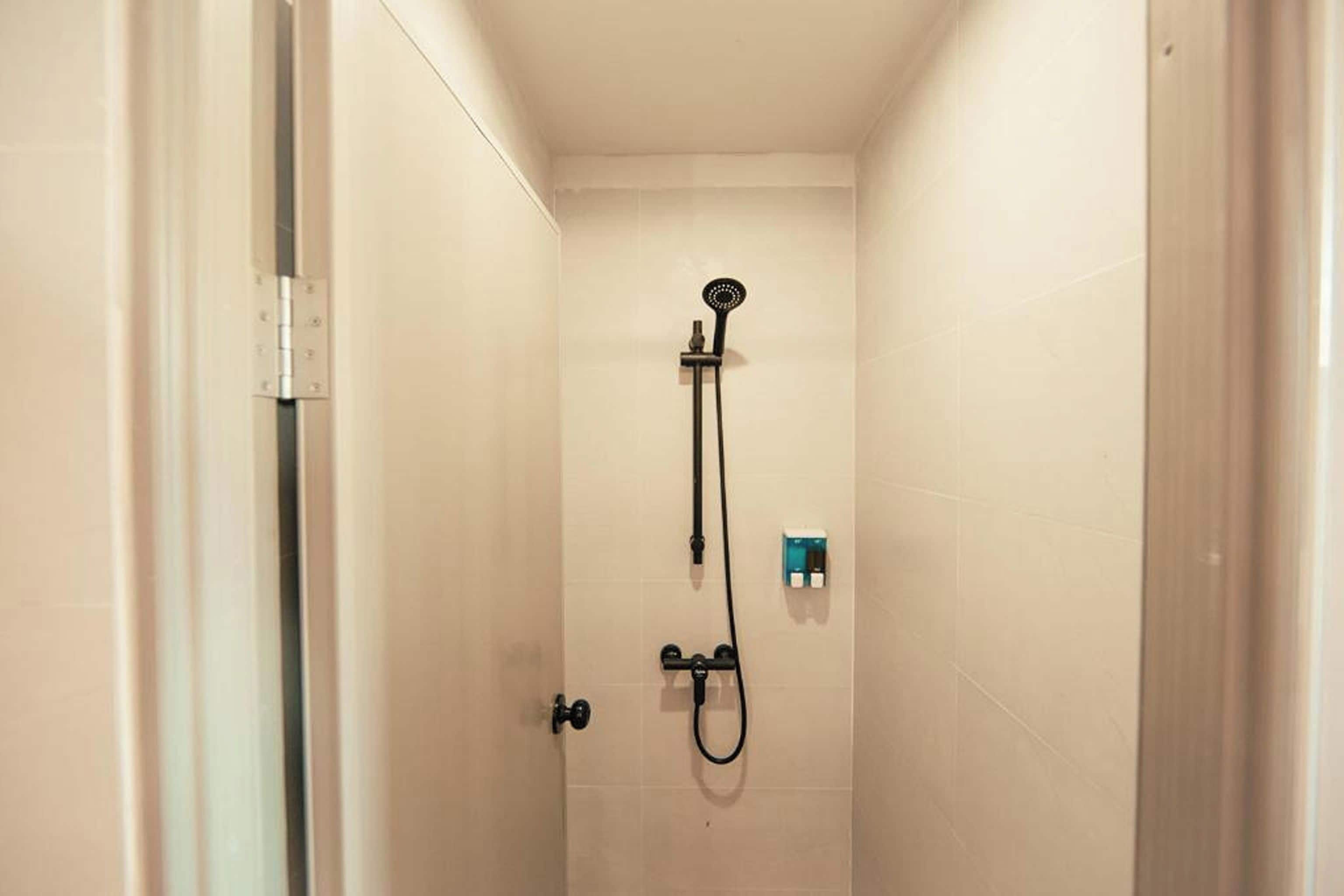 A small, enclosed shower area with a handheld showerhead and a wall-mounted control panel.