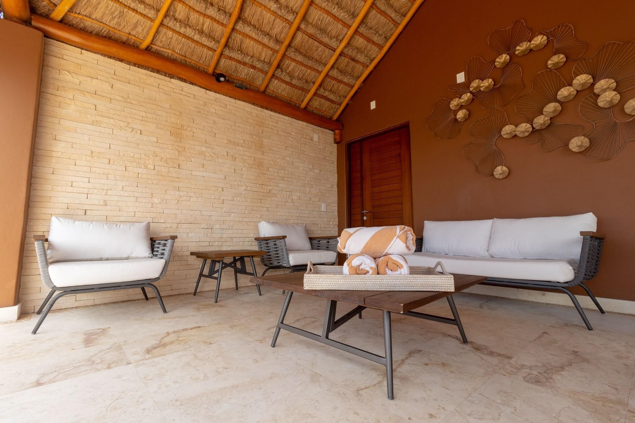 A room with a brick wall, a wooden ceiling, and a woven table. There are two sofas and two chairs.