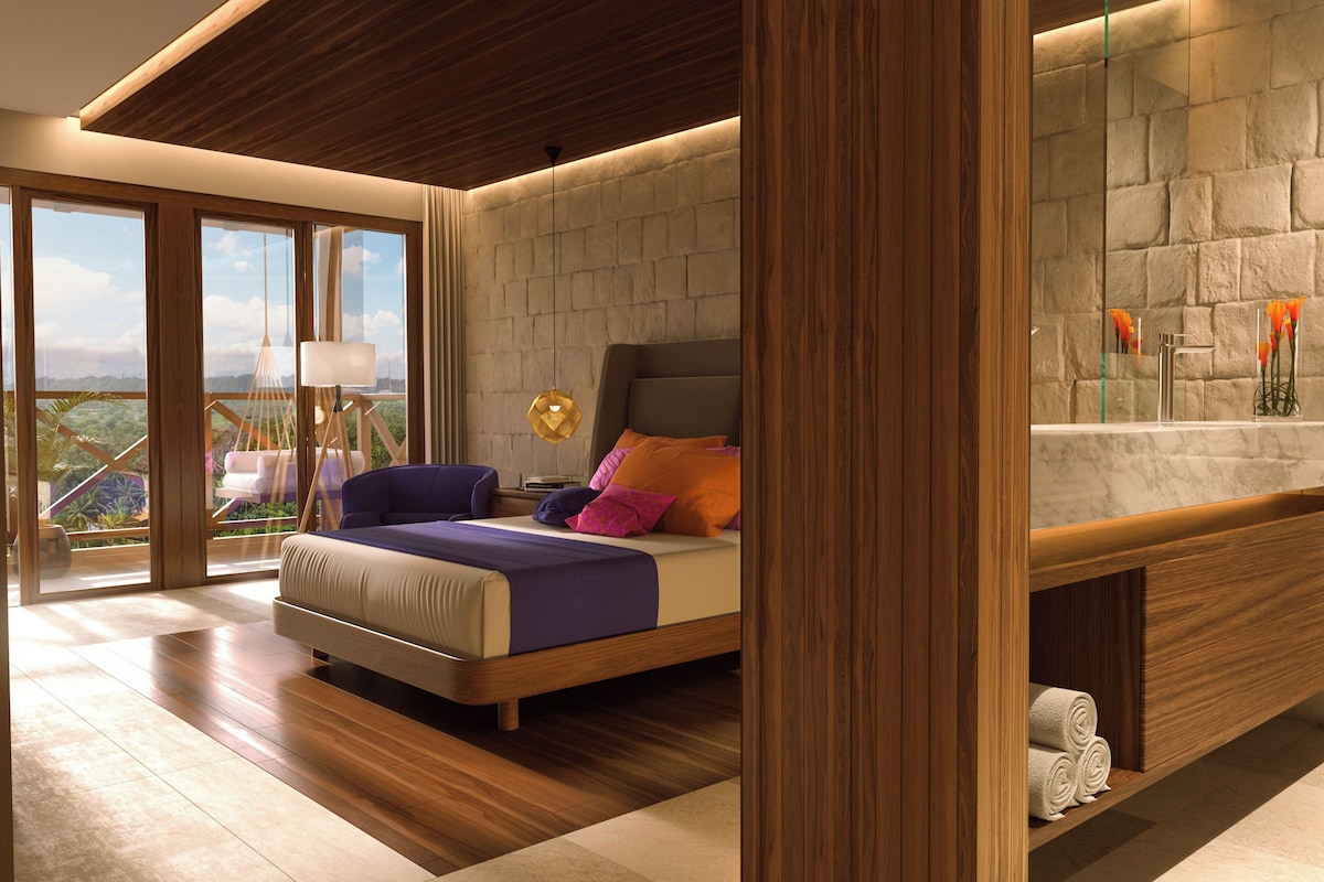 A modern bedroom with a bed, a nightstand, a large window with a view, and a stone wall.