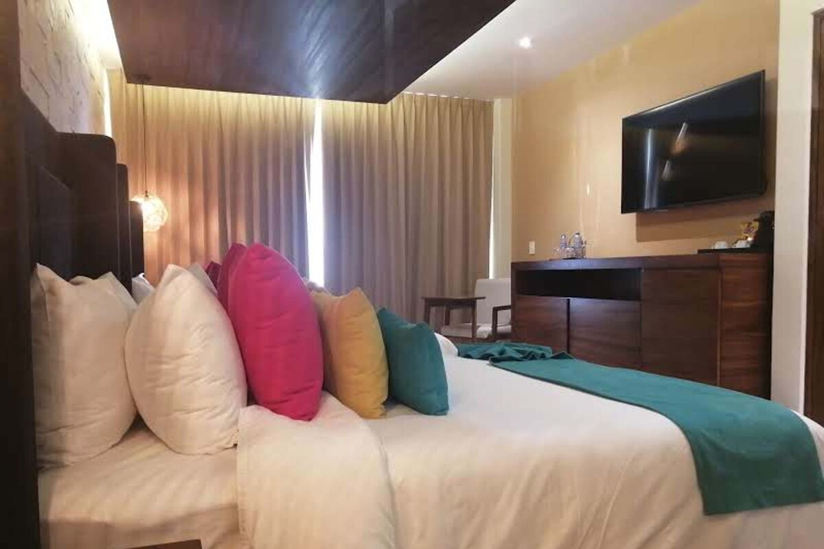 Habitación de hotel con cama, televisor, escritorio y ventana con cortinas.