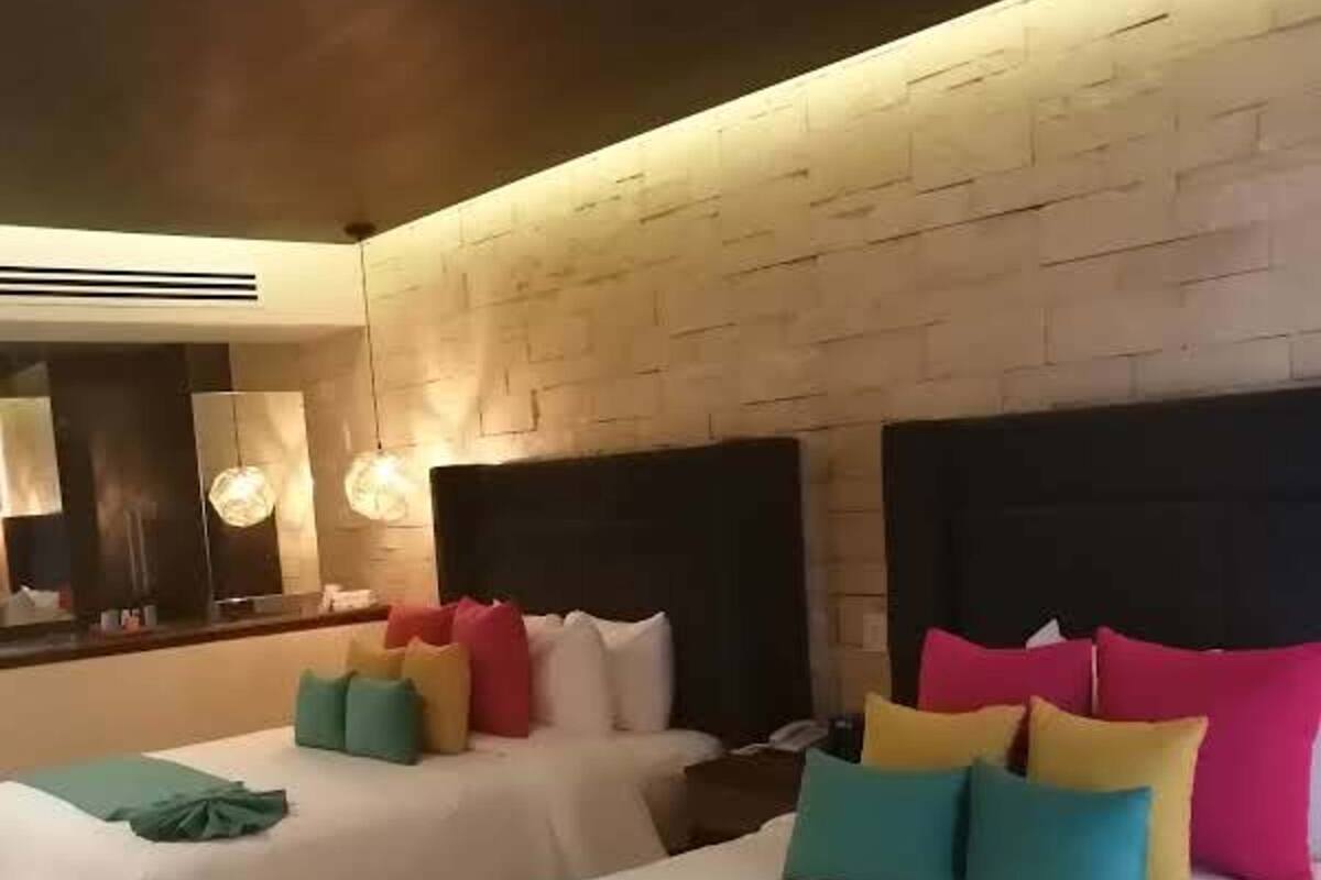 Quarto de hotel com duas camas, um espelho grande e design moderno.