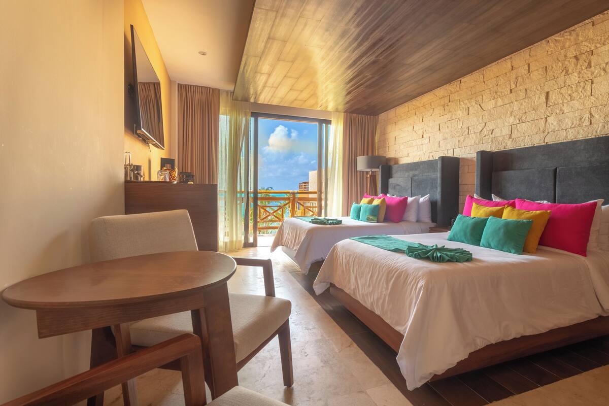 Quarto de hotel com duas camas, uma mesa de madeira e varanda com vista.