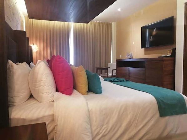 Habitación de hotel con cama, televisor, escritorio y ventana con cortinas.