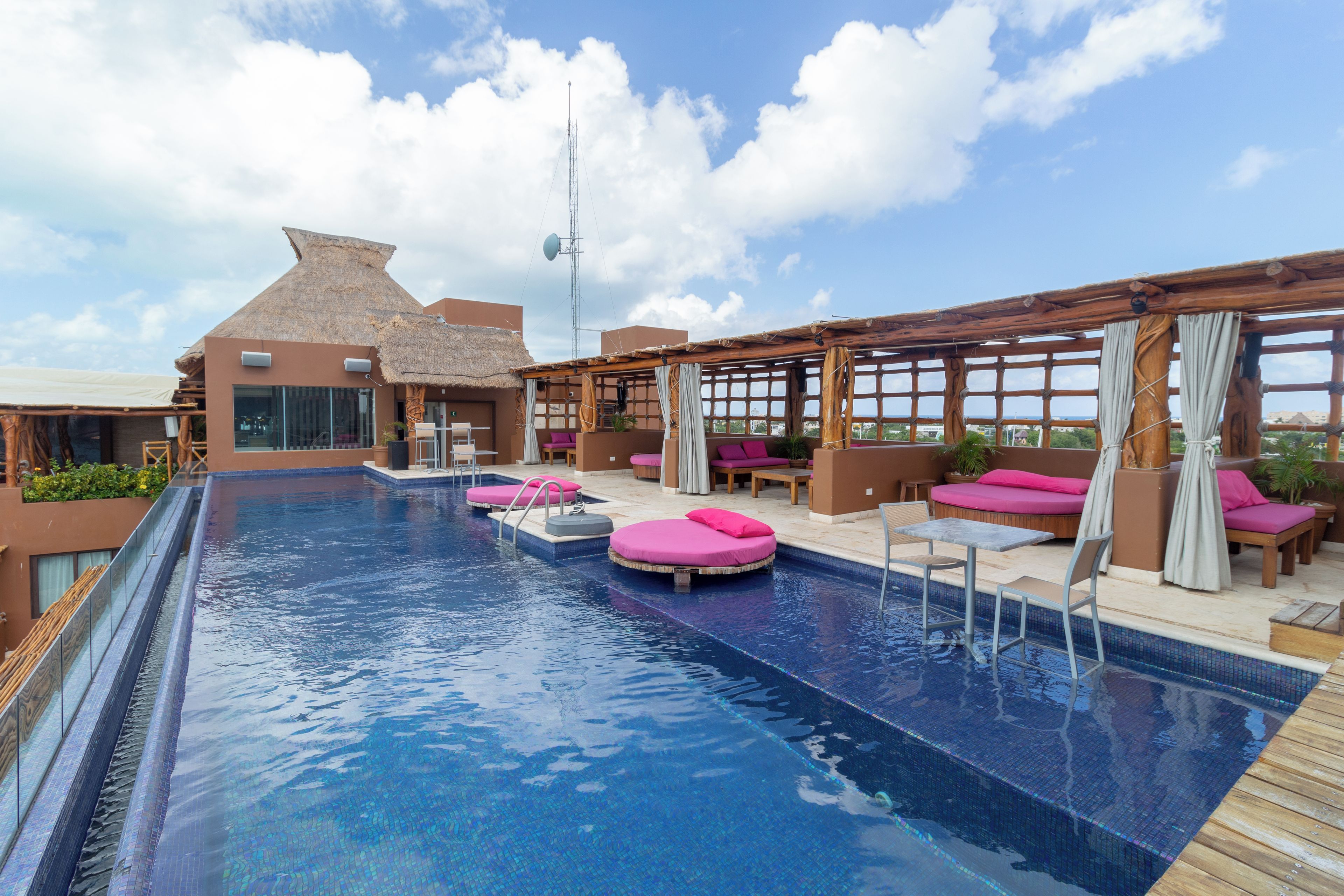 A rooftop infinity pool with lounge chairs and a thatched-roof building.