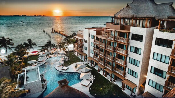 A resort with a pool, multiple balconies, and a view of the ocean at sunset. - Belo Isla Mujeres All Inclusive (Isla Mujeres)