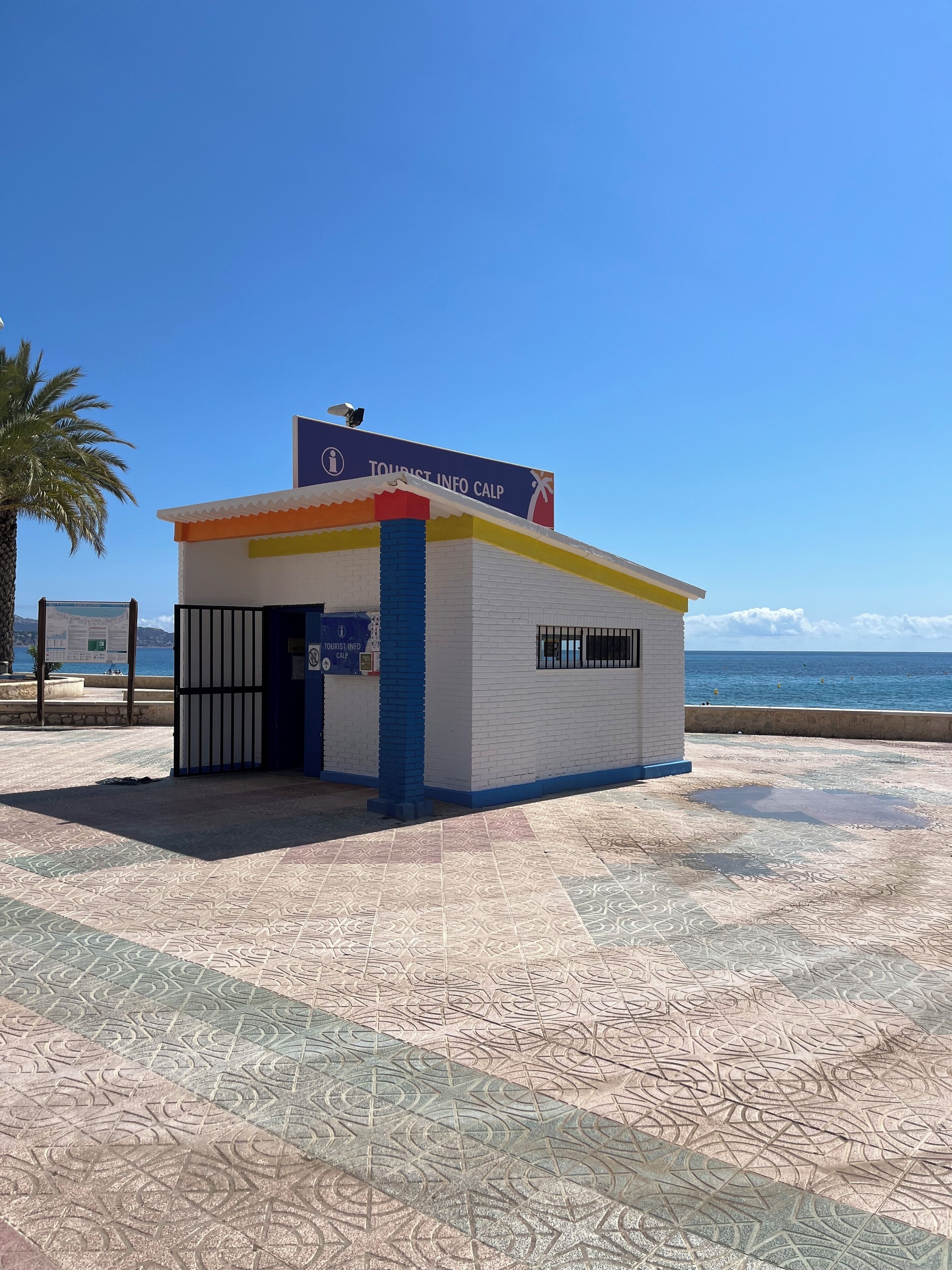 A small tourist information center with a blue and white exterior, located near a beach with a clear sky.