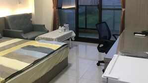 Habitación de hotel con cama, escritorio, silla, equipo de aire acondicionado y vista a edificios desde la ventana.