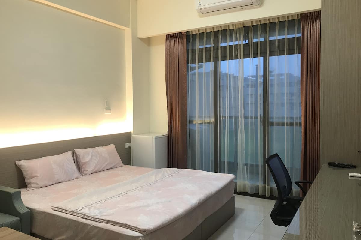 Habitación de hotel con cama, escritorio, aire acondicionado y vista a edificios a través del ventanal.