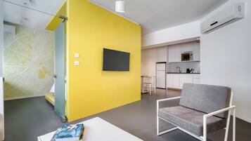 A modern living room with a yellow accent wall, a grey sofa, a flat-screen TV, and a white coffee table with books and a decorative item.