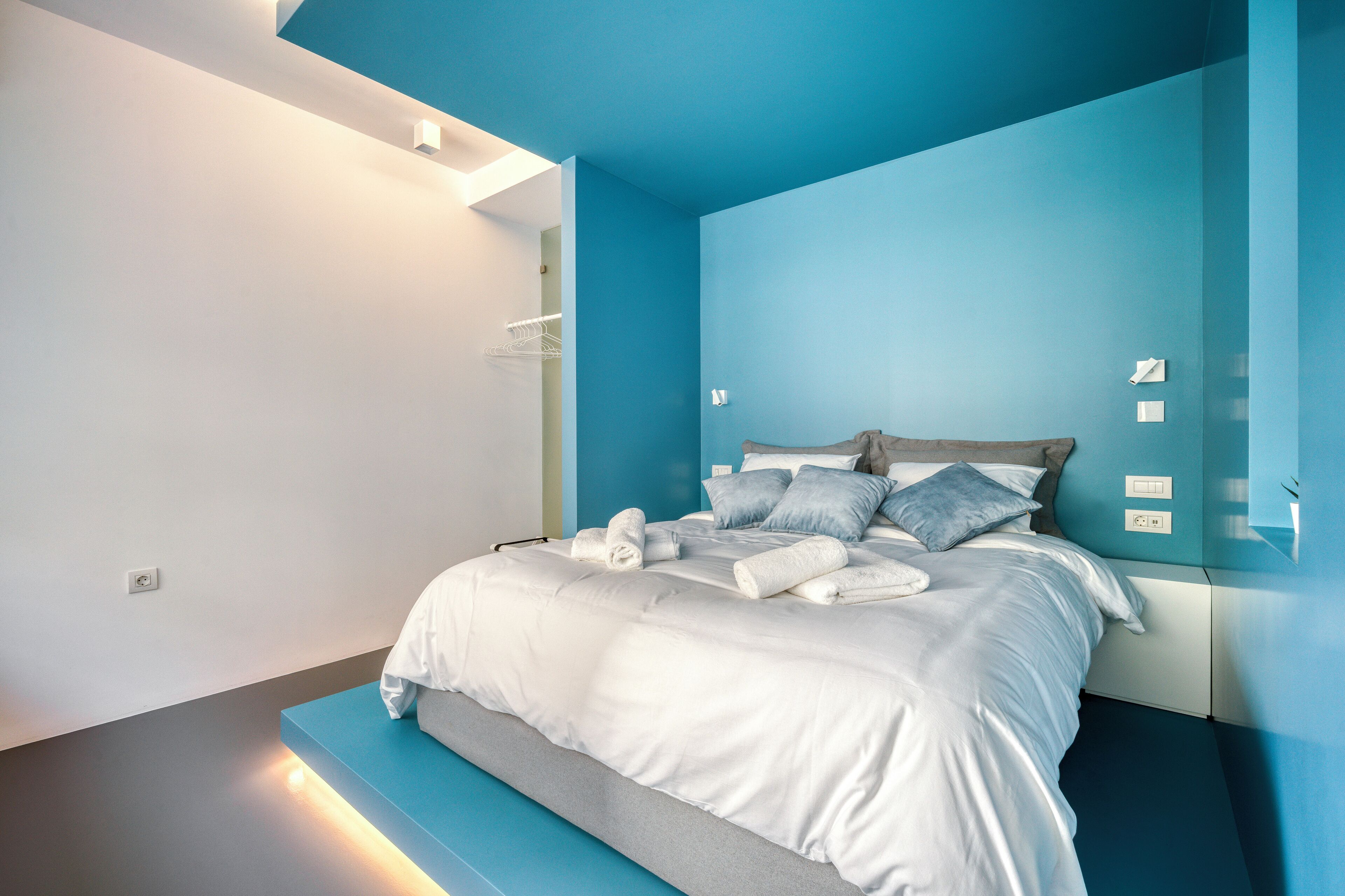 Un dormitorio moderno con cama, ropa de cama blanca y una pared de acento azul.