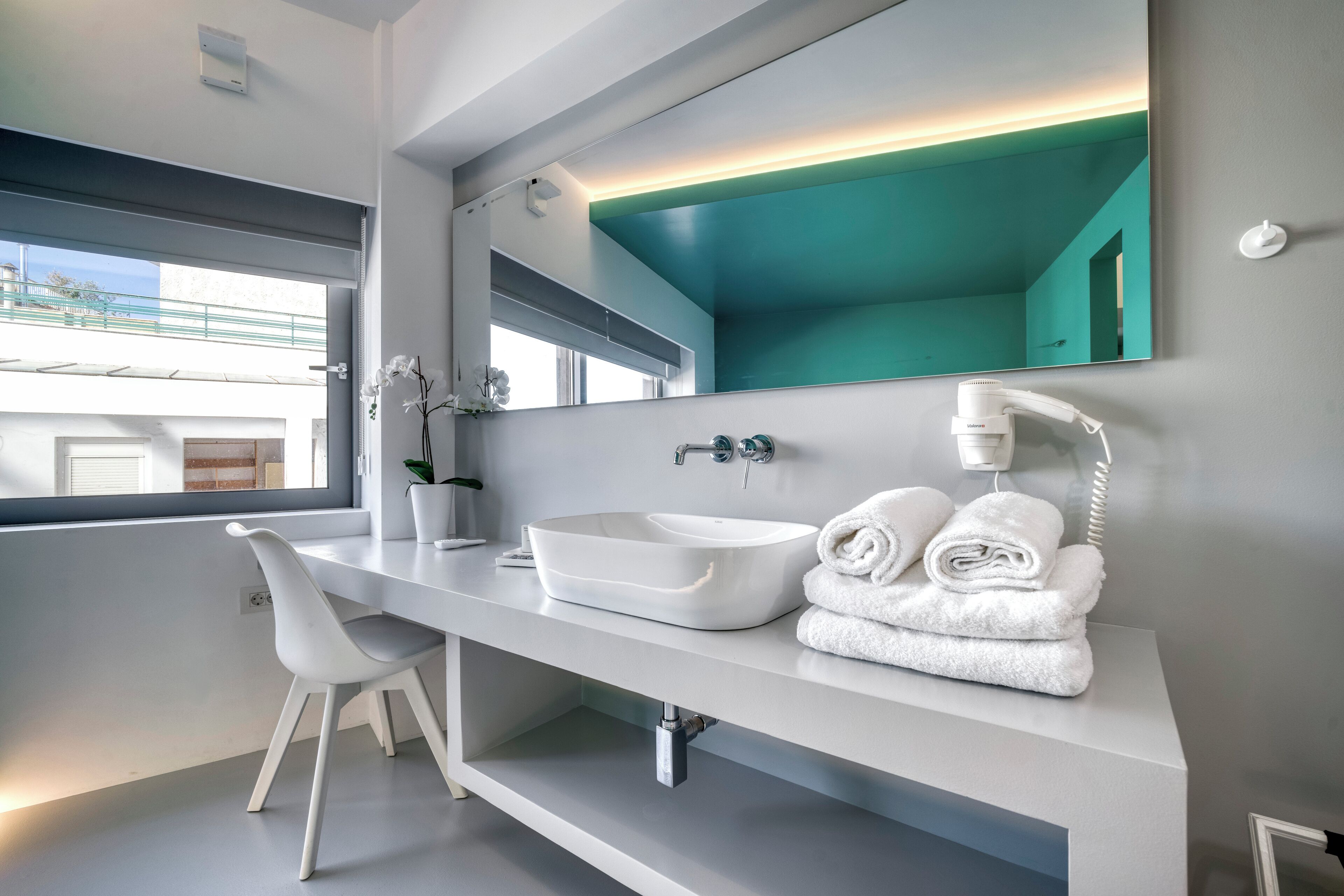 A modern bathroom with a white vanity, a large mirror, a white sink, and a towel rack.