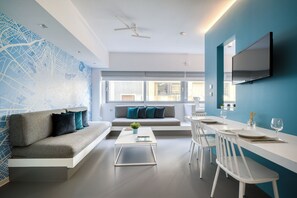 A modern living room with a sofa, coffee table, and dining area with chairs and a TV. - Athens Color Cube (Athens)