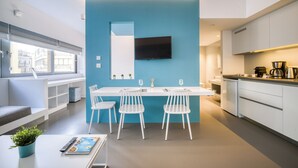 A modern kitchen with a blue accent wall, white cabinetry, and a flat-screen TV mounted above the counter. - Athens Color Cube (Athens)