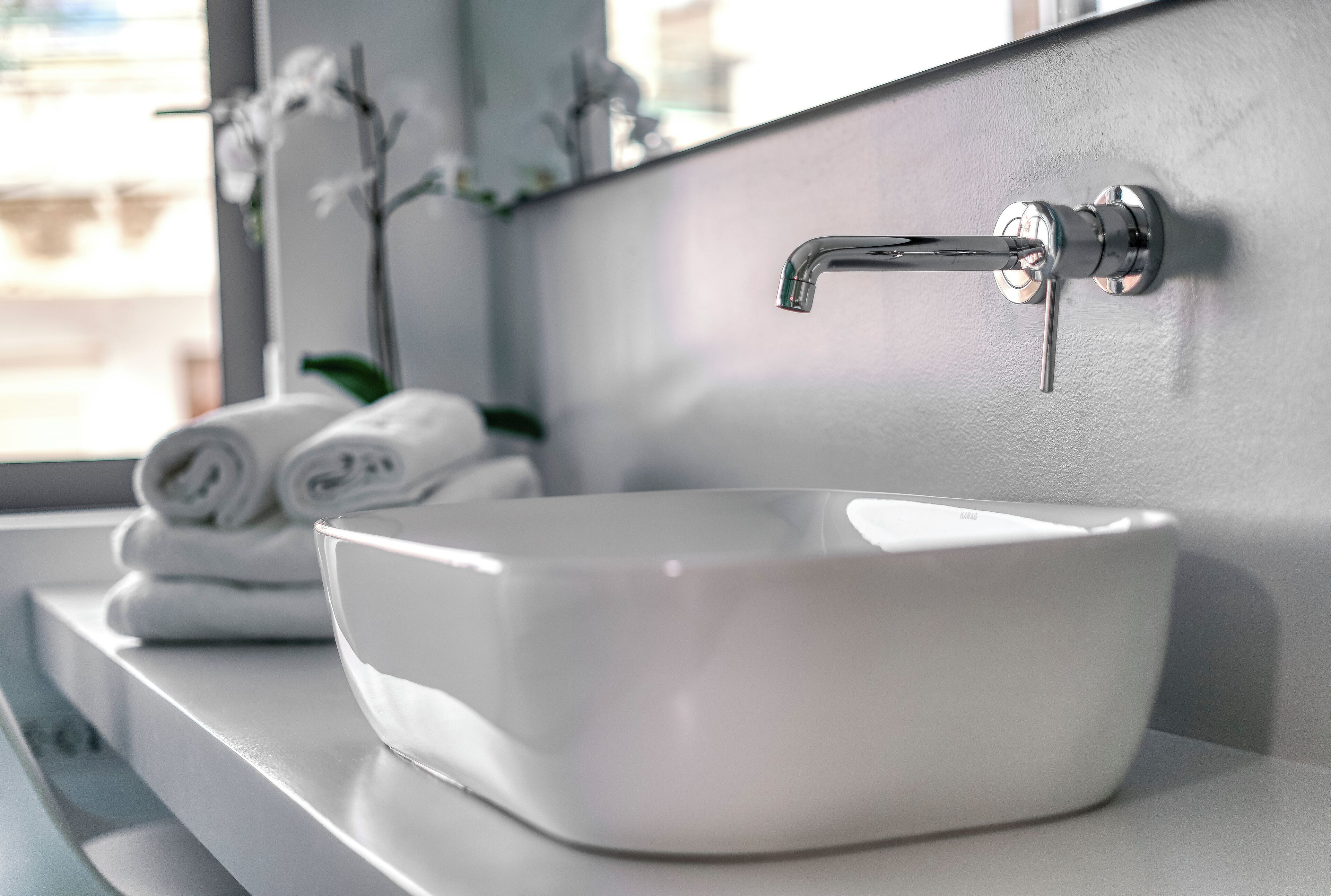 A white ceramic sink with a modern faucet, a mirror above it, and a window in the background.
